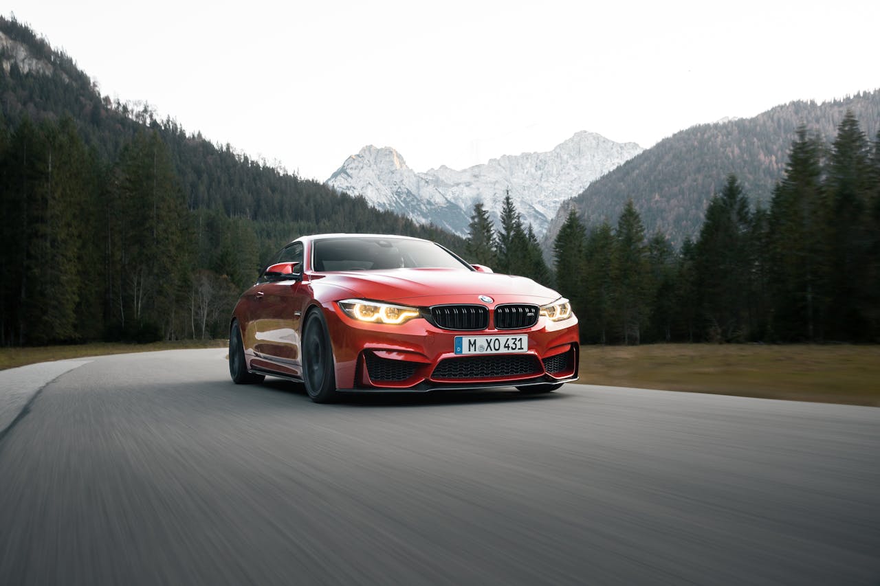 A stunning red BMW car speeds along a forest road with majestic mountains in the background.