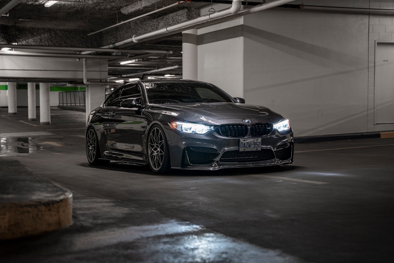A sleek black BMW parked in a dimly lit underground garage with illuminated headlights.